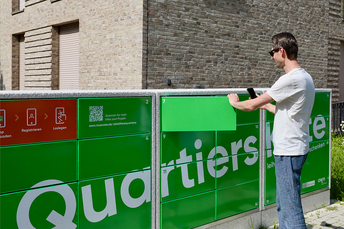 Ein Mensch vor einer grünen Ausleihstation mit der Aufschrift „Quartierskiste“
