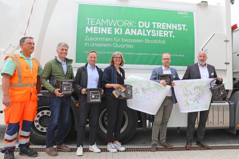 Sechs Personen stehen vor einem Schild, das sagt: "Teamwork: Du trennst. Meine KI analysiert."
